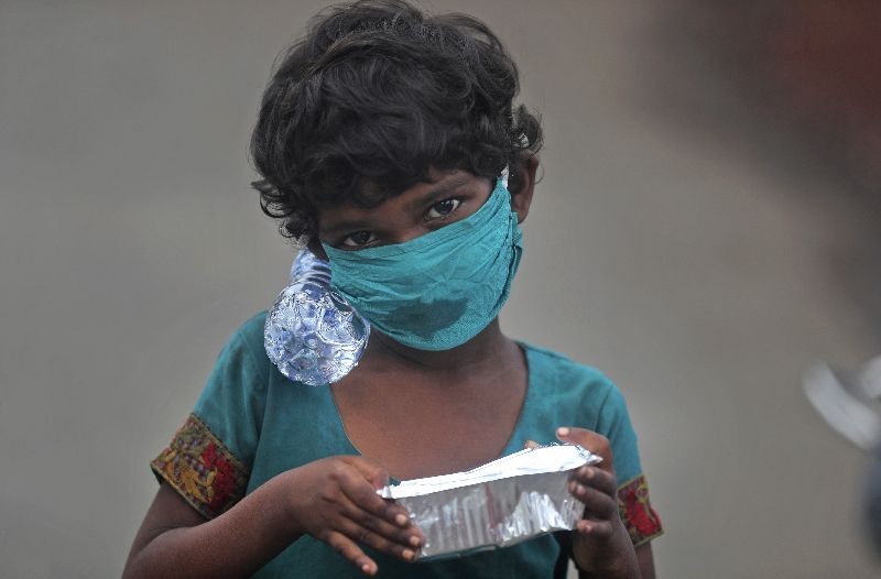 A girl wearing a face mask walks with a bottle of drinking water and a food packet that she received from a food distribution site in Mumbai, India. (Photo by Rafiq Maqbool/AP Photo)